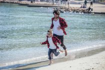 Padre e hijo corriendo a lo largo de la playa - foto de stock