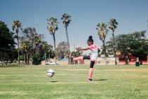 Colegiala pateando pelota de fútbol en el campo de deportes de la escuela - foto de stock