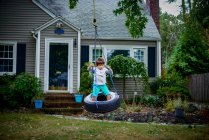 Menino brincando no pneu balançar no jardim — Fotografia de Stock