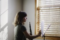 Mädchen mit Klarinette schaut auf Notenständer am Fenster — Stockfoto