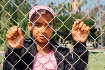 Portrait d'une écolière tenant une clôture métallique sur un terrain de sport scolaire — Photo de stock