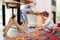 Die Mutter arbeitet am Küchentisch, während das kleine Mädchen auf dem Fußboden spielt. niedriger Schnitt — Stockfoto