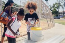 Écolières préparant des boissons de la boîte fraîche sur le terrain de sport scolaire — Photo de stock