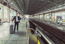 Далеких з видом на бізнесмена колісні валізи, стоять біля залізничного вокзалу — стокове фото