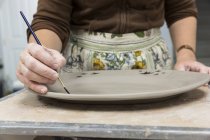 Female hands painting on clay platter — Stock Photo