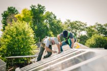 Dois trabalhadores que instalam painéis solares no telhado da casa — Fotografia de Stock