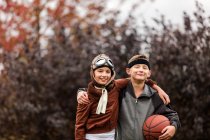 Retrato de niña y hermano gemelo usando trajes de jugador de baloncesto y piloto para Halloween en el parque - foto de stock