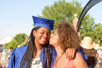 Mother kissing daughter on cheek at graduation ceremony — Stock Photo