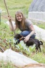 Frau mit Hund lächelt in Gemüsegarten in die Kamera — Stockfoto
