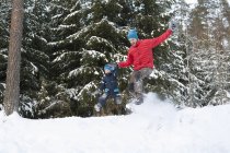 Man and son jumping from snow covered forest hill — Stock Photo