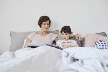 Mother and daughter lying on bed in light bedroom — Stock Photo