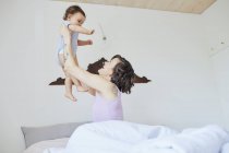 Мати сидить у ліжку і тримає дівчинку в повітрі — стокове фото