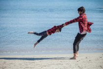Pai balançando filho ao redor na praia de areia — Fotografia de Stock