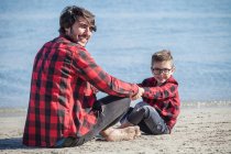 Padre e hijo sentados cara a cara en la playa - foto de stock