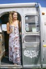 Young woman wearing maxi dress looking out from airstream doorway — Stock Photo