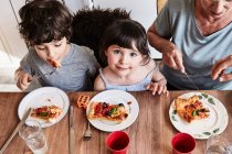 Nonna seduta al tavolo della cucina con nipoti, mangiare pizza, vista sopraelevata — Foto stock