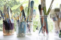 Fila de frascos con variedad de pinceles para artistas en el alféizar de la ventana del estudio de artistas - foto de stock