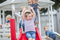 Хлопчики і дівчатка в дошкільному закладі, катаються на дитячому майданчику слайд в саду — стокове фото