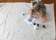 Overhead view of female artist sitting on dust sheet finger painting abstract canvas — Stock Photo