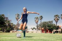 Schoolgirl soccer player kicking ball on school sports field — Stock Photo