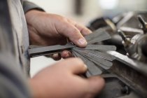 Mani di meccanico di auto maschile in possesso di etichette metalliche in garage di riparazione — Foto stock