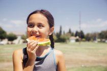 Schoolgirl eating melon slice on school sports field — Stock Photo