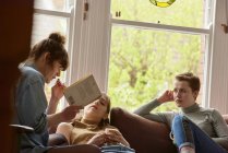 Три друзі-жінки читають книгу на дивані — стокове фото