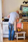 Visão traseira da menina nas fezes assistindo pai preparando comida na cozinha — Fotografia de Stock
