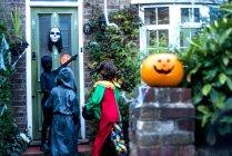Три мальчика в костюмах на Хэллоуин, стоят у дверей, дают сладости или сладости, вид сзади — стоковое фото