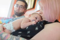 Donna con bambino sul petto, marito sullo sfondo — Foto stock