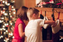 Irmão e irmã procurando presentes em meias no Natal — Fotografia de Stock