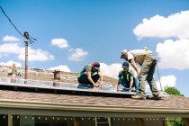Tres trabajadores instalando paneles solares en el techo de la casa, vista de ángulo bajo - foto de stock