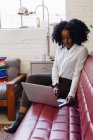 Афро-американська жінка в офісі сидить на дивані за допомогою ноутбука — стокове фото