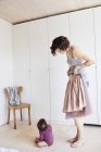 Mother holding skirt while baby girl sitting on floor — Stock Photo