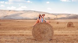 Friends sitting back to back on top of hay bale — Stock Photo