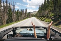 Road trip couple driving convertible on rural highway with hands raised, Breckenridge, Colorado, USA — Stock Photo