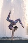 Teenage girl beside fountain balancing on hands in yoga position — Stock Photo