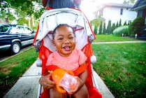 Menina feliz em cadeira de empurrar na calçada suburbana, retrato — Fotografia de Stock