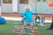 Mädchen im Kindergarten springt über Plastikreifen im Garten — Stockfoto