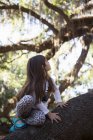 Девушка сидит на ветке дерева и смотрит вверх — стоковое фото