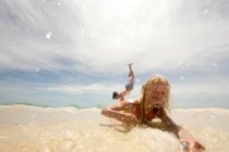 Девушка лежит на пляже на мелководье, брат делает стойку на руках на заднем плане — стоковое фото