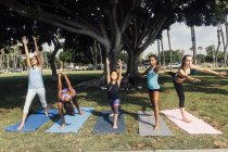 Niñas y adolescentes practicantes de yoga guerrero posan en el campo de juego de la escuela - foto de stock