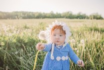 Baby girl in field, holding dandelion — Stock Photo