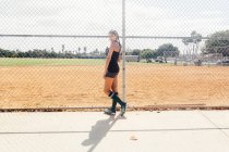 Portrait of schoolgirl soccer player at wire fence on school sports field — Stock Photo