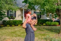 Взрослая женщина в саду с маленькой дочерью на плечах, портрет — стоковое фото