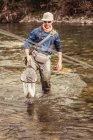 Joven pescador arrodillado en el río llevando pescado capturado en la red, Mozirje, Brezovica, Eslovenia - foto de stock