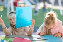 Dos chicas jóvenes, al aire libre, dibujo, niña sosteniendo obras de arte - foto de stock