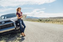 Frau lehnt mit Karte an Auto — Stockfoto