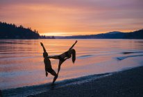 Couple practising yoga on beach at sunset — Stock Photo