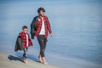Батько і син бігають уздовж пляжу, носячи куртки над плечем — стокове фото